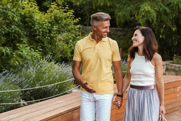 Portrait of smiling middle-aged couple man and woman holding hands together while walking in summer park