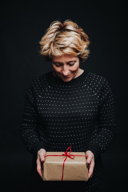 Foto ritratto di donna di mezza età sorridente che guarda le mani che tengono presente isolato su sfondo nero