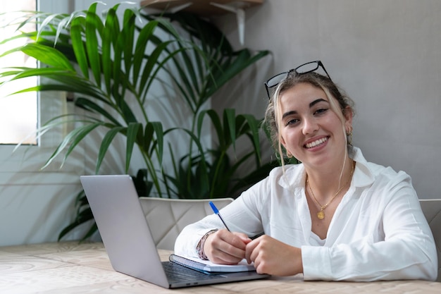 Portrait of smiling millennial caucasian female student sit at desk at home study online on laptop h