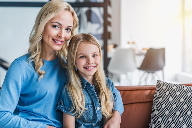 Portrait of smiling mom with little kid daughter on sofa at home