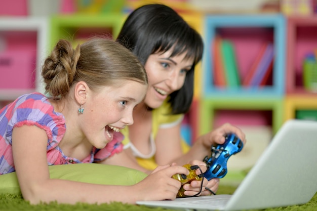 Portrait of smiling mother and daughter using laptop playing video game