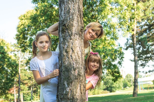 Foto ritratto di una madre sorridente con le figlie in piedi vicino a un albero nel parco