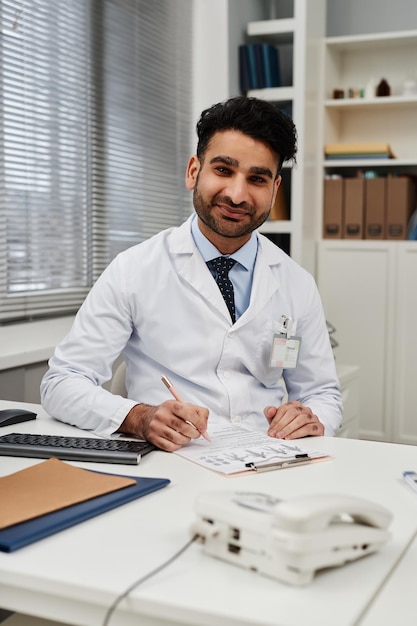 Foto ritratto di un medico musulmano sorridente alla scrivania che guarda la telecamera