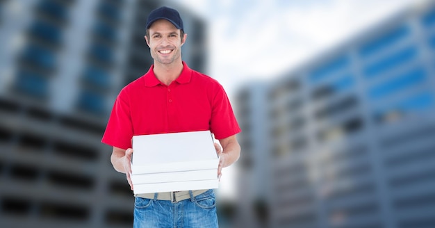 Portrait of smiling pizza delivery man holding pizza box against buildings