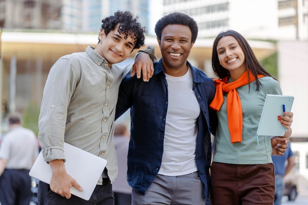 Foto ritratto di giovani studenti positivi sorridenti che si abbracciano in piedi guardando la macchina fotografica sulla strada