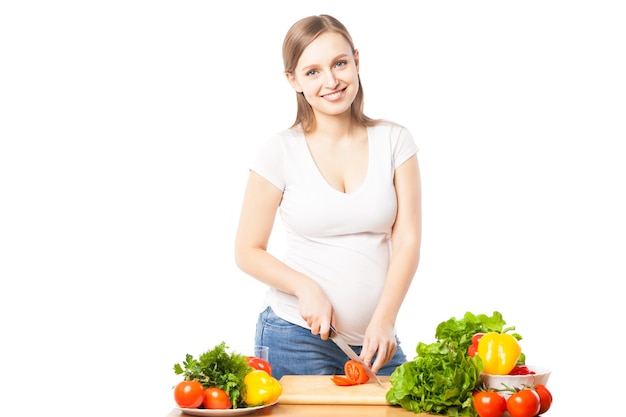 Portrait of smiling pregnant woman cutting vegetable on board.White background