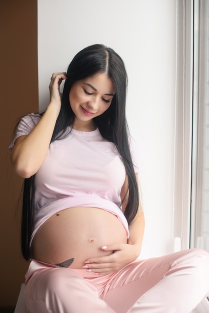 Portrait of smiling pregnant woman sit in window sill