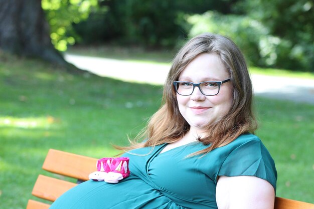 Photo portrait of smiling pregnant woman sitting on bench at park