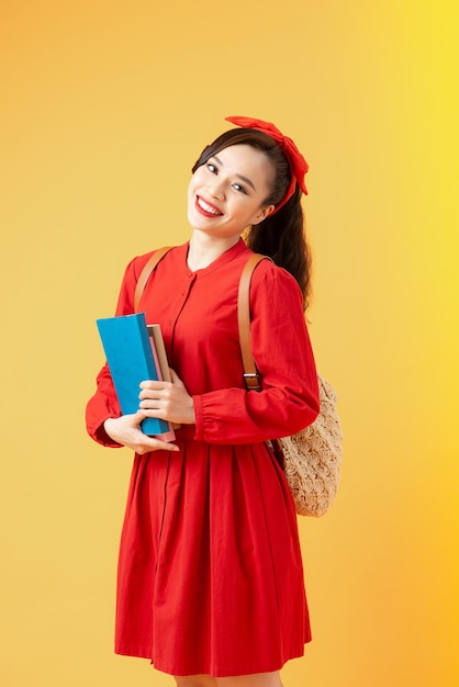 Portrait of a smiling pretty asian girl holding books and looking at camera isolated