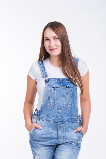 Portrait of a smiling pretty woman in denim overall isolated on white wall