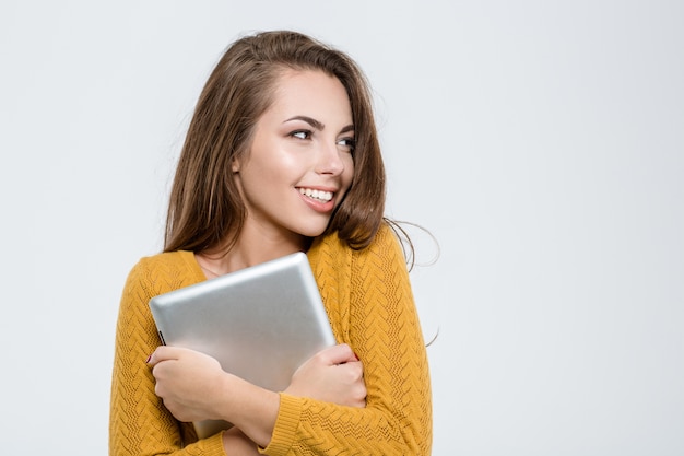 Portrait of a smiling pretty woman holding tablet computer and looking away isolated on a white background