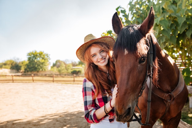 Ritratto di cowgirl sorridente piuttosto giovane donna con cappello con il suo cavallo