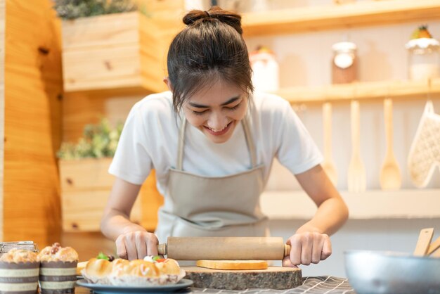 キッチンのテーブルで自家製のベイククッキーとケーキの材料のための生地で料理を楽しんでいる笑顔のプロの美しさのアジアの女性シェフの肖像画