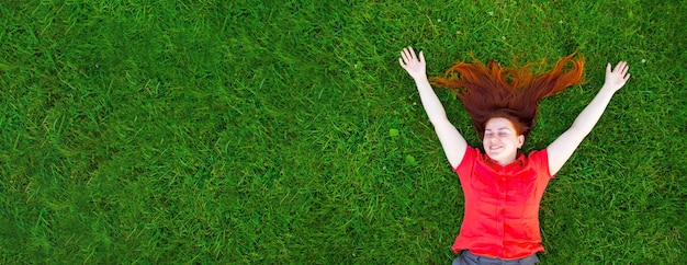 Portrait of a smiling redhaired young girl on green grass outside in park