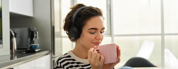 portrait of smiling relaxed woman drinks warm tea and listens music or ebook in kitchen