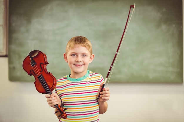 Portrait of smiling schoolboy holding violin in classroom