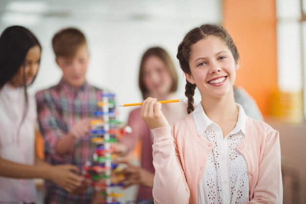 Portrait of smiling schoolgirl holding pencil in classroom