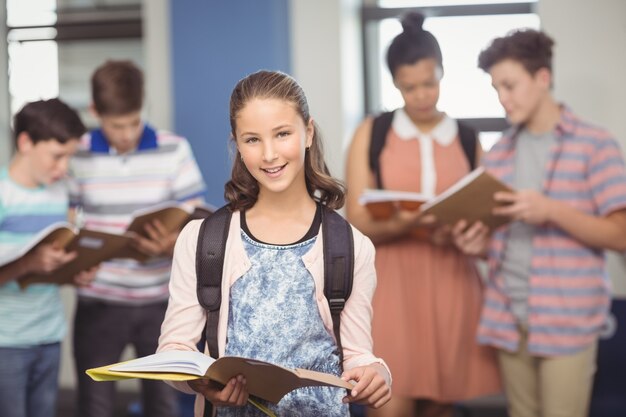 Портрет улыбающейся школьницы, стоящей с книгой в классе