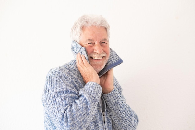Портрет улыбающегося пожилого бородатого мужчины на изолированном белом фоне, закрывающего лицо синим свитером и смотрящего в камеру