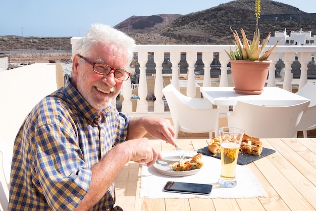 Foto ritratto di un uomo anziano sorridente che mangia mentre è seduto sul balcone
