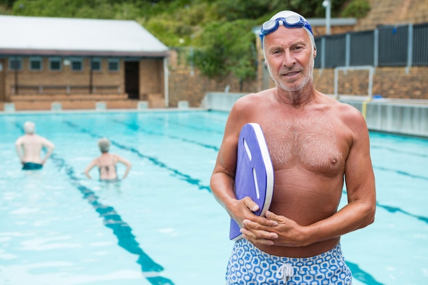 Портрет улыбающегося старшего мужчины, держащего доску у бассейна