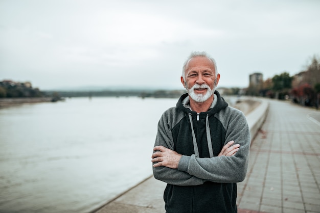 Foto ritratto di uomo anziano sorridente in una felpa con cappuccio sulla banchina della città. guardando la fotocamera