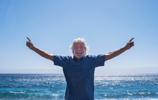 Photo portrait of smiling senior man with arms outstretched standing at beach