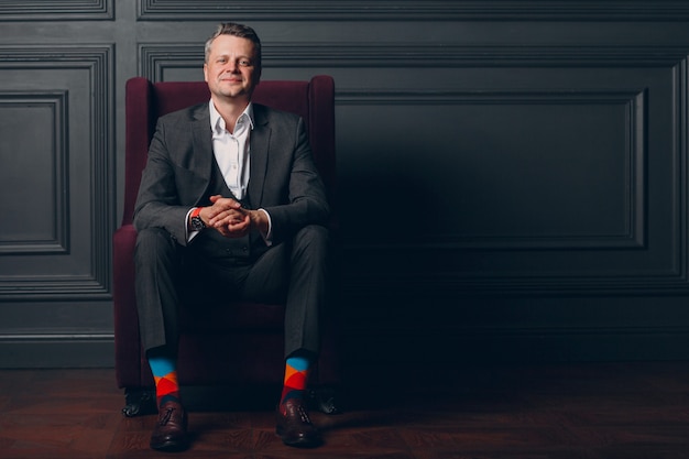 Portrait of smiling senior middle adult man in gray suit and colorful multi colored socks looking at camera with copy space.