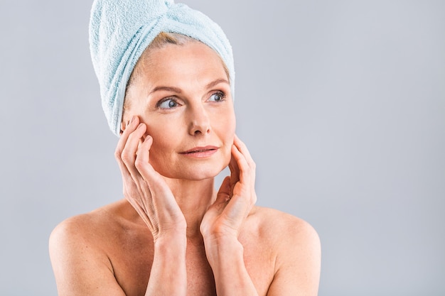 portrait of smiling senior woman feeling soft skin with hand after spa bath mature woman draped in towel on body and wet hair looking at camera