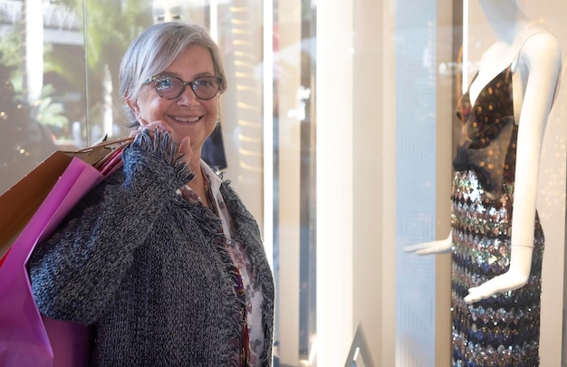 Photo portrait of smiling senior woman holding shopping bag standing in shopping mall