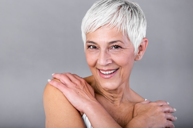 Portrait of a smiling senior woman looking at camera. closeup face of mature woman after spa treatment isolated over grey background. anti-aging concept.