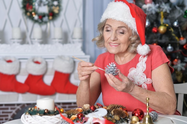 Portrait of smiling senior woman in Santa hat holding pine cone decoration