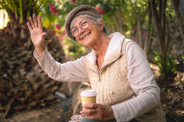 Portrait of smiling senior woman sitting in the park enjoying nature holding a takeaway coffee cup