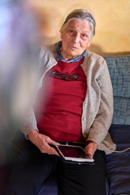 Photo portrait of smiling senior woman using digital tablet on sofa