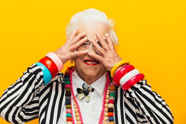 Portrait of smiling senior woman with hands on face against yellow background