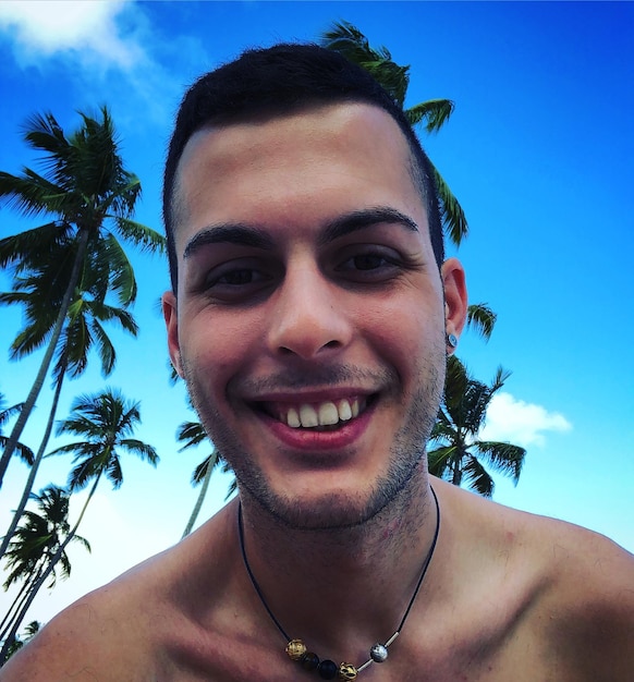 Portrait of smiling shirtless man against blue sky