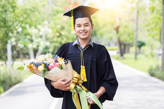 Portrait of smiling student wearing graduation gown while holding bouquet outdoors