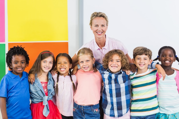 Портрет улыбающегося учителя и дети, стоя вместе с руки вокруг