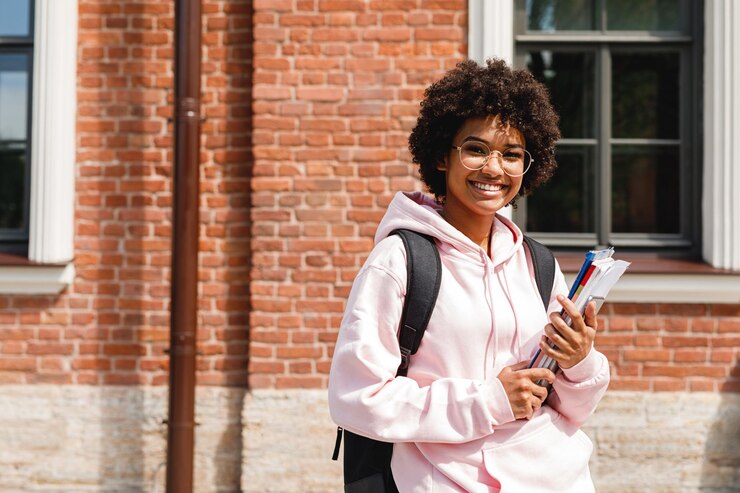 Photo portrait of smiling teenage girl holding books against brick wall