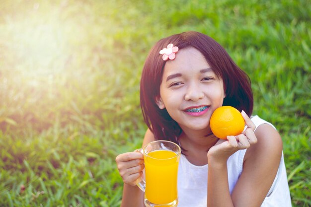 Portrait of smiling teenage girl holding fruit and juice while sitting on grass