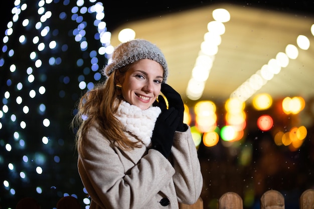 Portrait of smiling teenager wearing winter clothes outdoors. Christmas lights in the background.