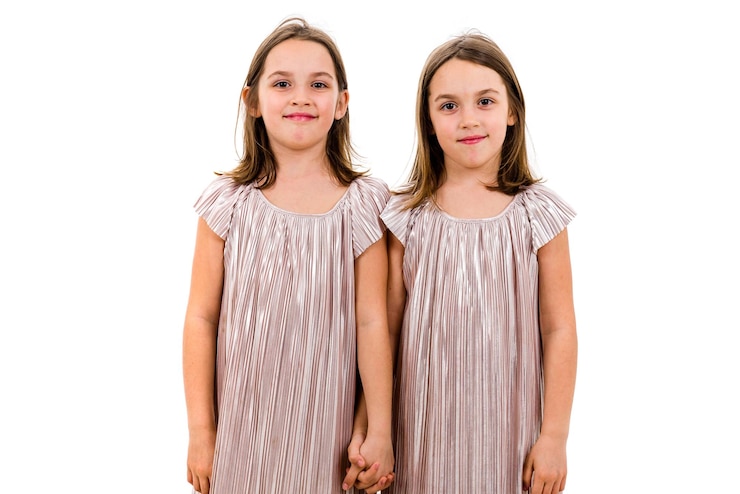 Photo portrait of smiling twins holding hands standing against white background