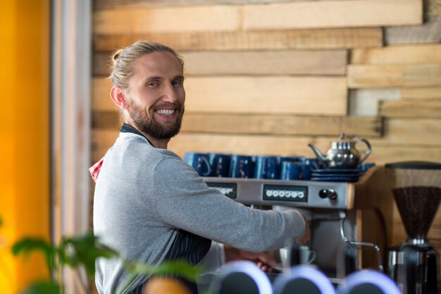 Ritratto del cameriere sorridente che produce tazza di caffè