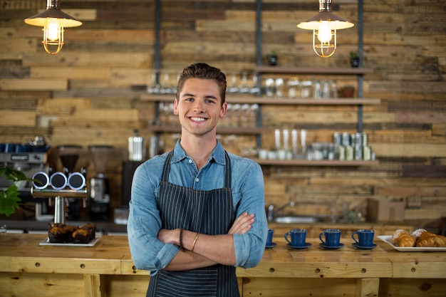 Portrait of smiling waiter standing with arms crossed