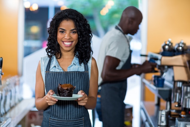 Portrait of smiling waitress holding a plate of cupcake