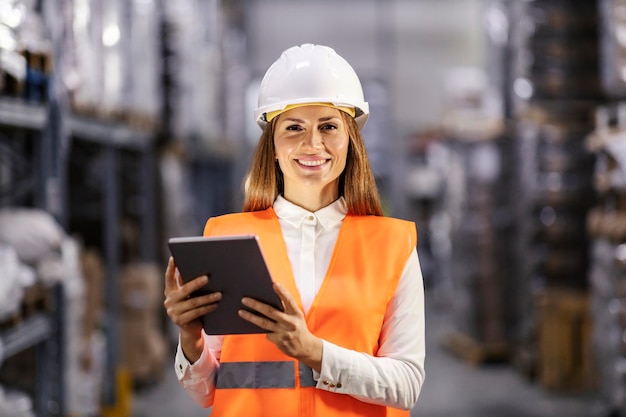 Portrait of a smiling white collar worker standing with tablet in storage and smiling at the camera