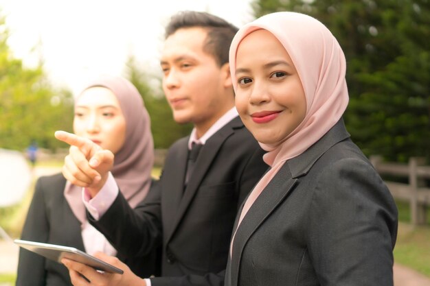 Portrait of smiling woman by colleagues using digital tablet in park