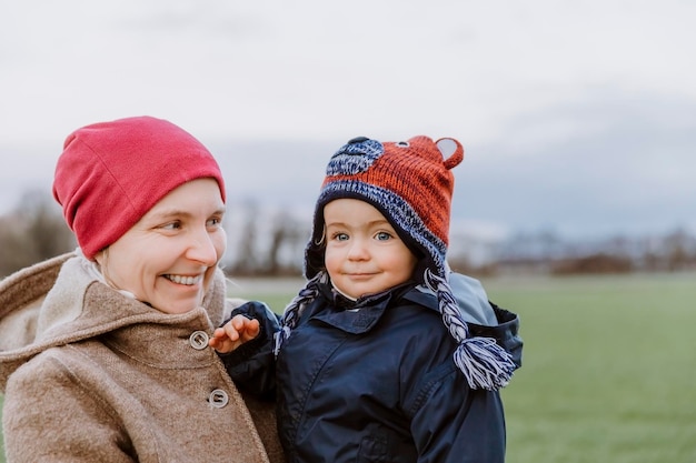 portrait of smiling woman carrying baby girl in park during winter
