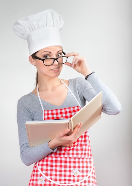 Portrait of smiling woman in chief's hat with the cookbook raising the index finger up