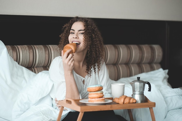 Photo portrait of smiling woman eating croissant at home